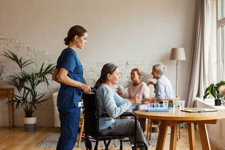 Adult child and older parent share tea beside family photos in a comfortable assisted living room.